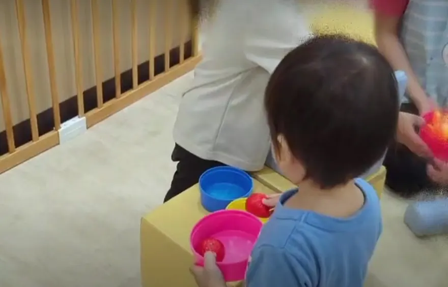 保育室でカラフルな器を手に取ってあそぶ子どもと保育士