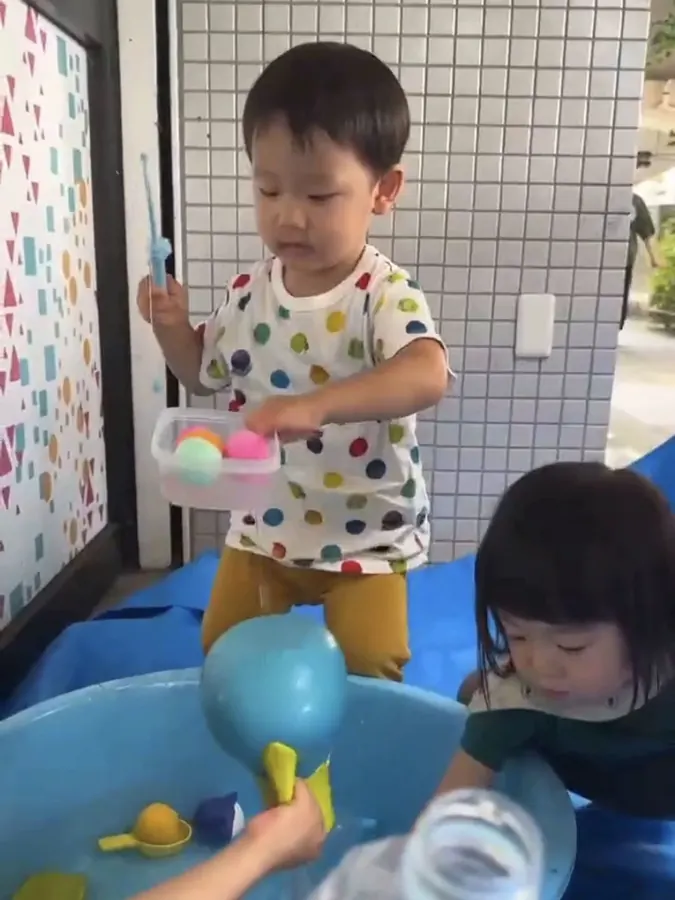 タライのそばに立って水あそびに夢中になっている子ども